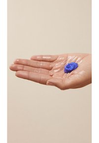 Blå kräm ligger på en öppen, något fuktig hand. Huden är ljus med synliga detaljer av handflatan och fingrarna, mot en neutral bakgrund.