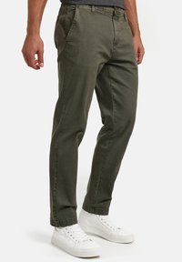 Pantalones verde oliva de corte recto, fabricados en un tejido ligero y con bolsillos frontales. Combinados con zapatillas blancas.