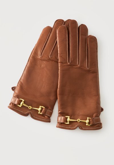 Paire de gants en cuir marron avec couture blanche et détails de boucles métalliques dorées sur un fond clair.
