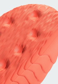 Textured rubber shoe sole in bright coral, featuring raised dots and grooves for grip. Slight sheen visible on the surface.