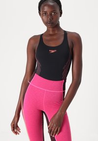 Black swimsuit with orange accent lines and a high-neck design, paired with high-waisted pink leggings featuring contrasting side panels.