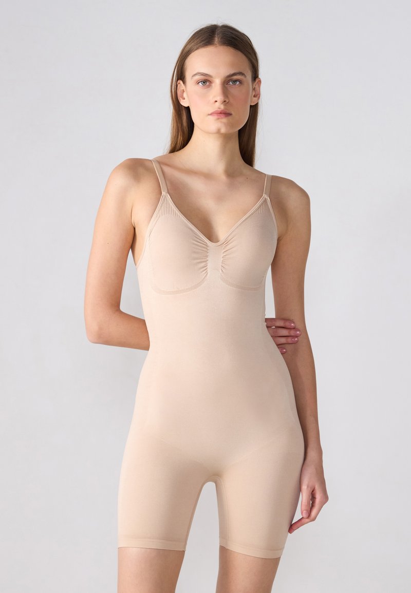 Beige fitted bodysuit with adjustable spaghetti straps, v-neckline, gathered detail at bust, and mid-thigh length. Smooth, stretchy fabric.