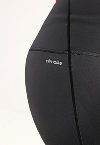 Leggings sportivi neri realizzati in tessuto elasticizzato. Presentano un'etichetta "climalite" discreta e una texture elegante e liscia senza motivi.