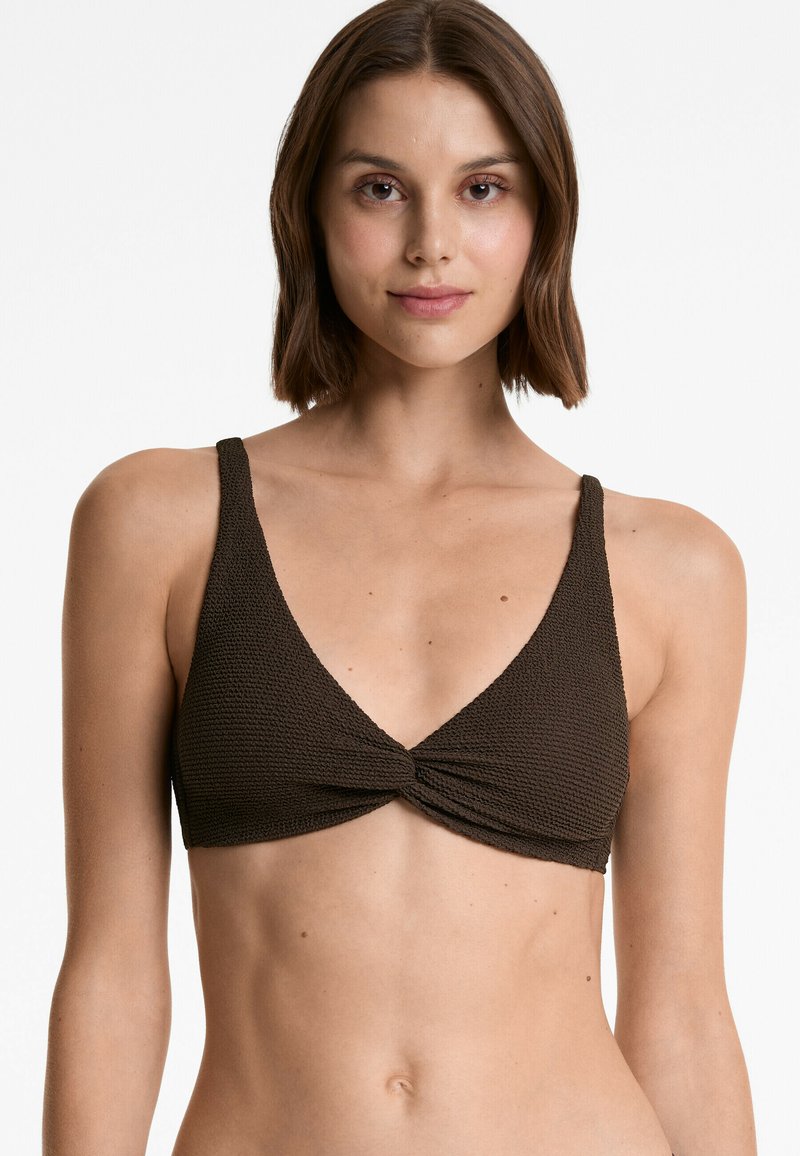 Bralet dintr-un material texturat de culoare maro, cu un decolteu adânc în V și un detaliu răsucit în față. Bretelele ajustabile îmbunătățesc potrivirea și confortul. Finisajul materialului este neted.