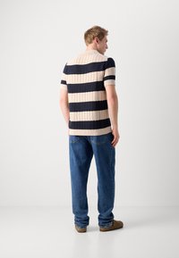 Polo shirt tricotat cu dungi în nuanțe de bej și bleumarin, cu un model texturat, mâneci scurte și guler ribatit; asortat cu blugi din denim bleumarin.