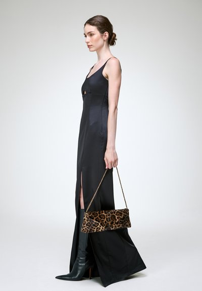 Femme en longue robe noire avec une fente latérale, bottes noires, tenant une pochette imprimé léopard avec une chaîne dorée.