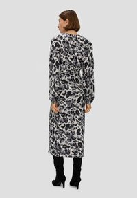 Langärmliges Kleid mit einem schwarz-grauen Leopardenmuster, aus leichtem Stoff gefertigt. Es hat eine taillierte Taille und reicht bis zur Mitte der Waden. Schwarze High-Heel-Stiefel.