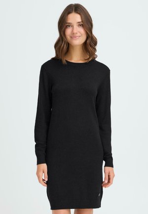 Svart långärmad strickklänning med rund halsringning, slät textur, figurnära silhuett och sidofållaccent. Enkelt och mångsidigt design.