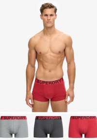 Boxers en coton rouges avec une ceinture noire "SUPERDRY", présentés aux côtés d'options grises et gris foncé avec des éléments de design similaires.