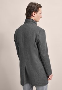 Grauer Wollmantel mit hohem Kragen, geradem Schnitt und seitlichen Schlitzen; verfügt über einen strukturierten Stoff und eine glatte Oberfläche.