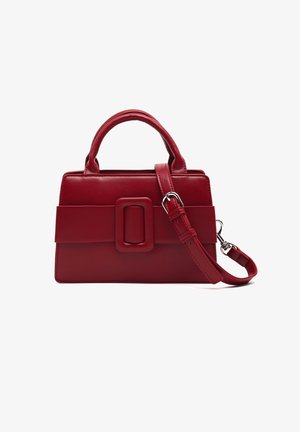 Bolso de piel roja con forma rectangular, que presenta un gran accesorio de hebilla y dos asas. Incluye una correa desmontable.