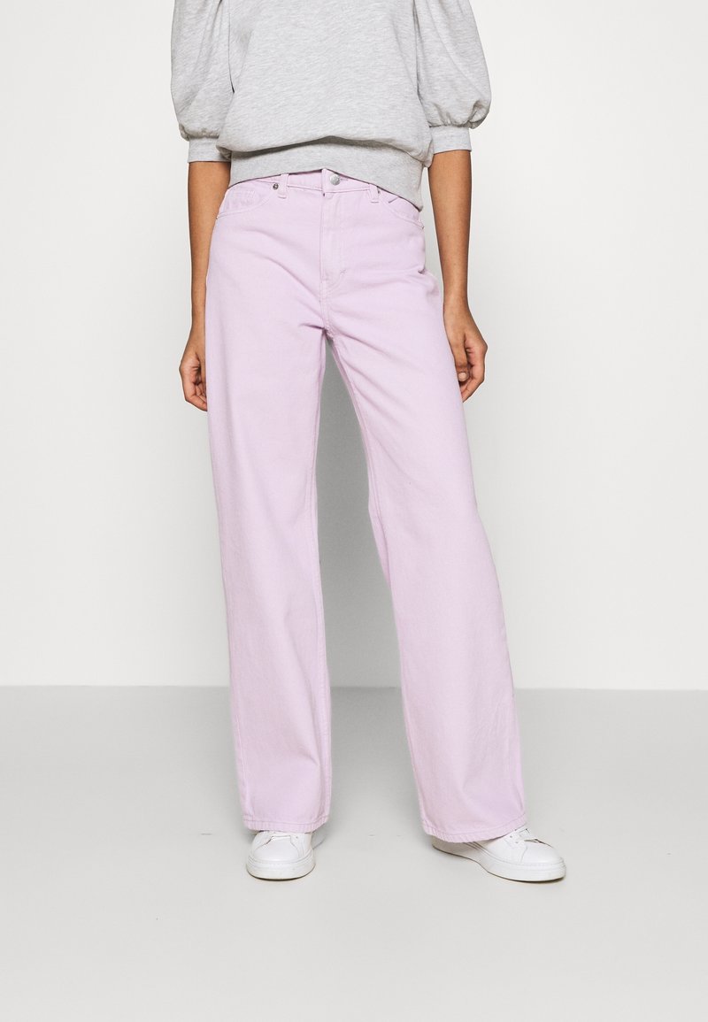 Jeans a gamba larga lavanda realizzati in denim con cinque tasche, passanti per cintura e chiusura frontale con bottone, abbinati a un sweatshirt grigio con maniche a sbuffo.
