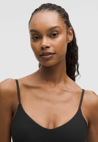 Black camisole with thin straps, smooth texture, and a deep V-neckline. Model has medium-length curly hair and natural makeup.