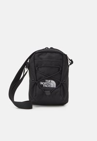 Black crossbody bag made of durable material. Features a logo, zip closure, adjustable strap, and elastic bungee detailing on the front.