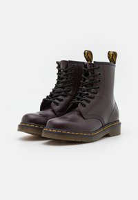 Par de botas de cuero marrón oscuro con cordones, con costuras amarillas y tiradores de marca, sobre un fondo blanco.
