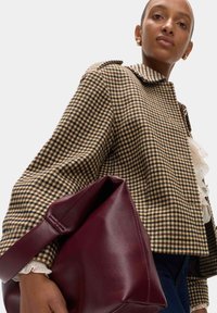 Bruine en crème houndstooth jas met een kraag, gecombineerd met een bordeauxleren tas met een slonzig ontwerp en een dikke schouderband.