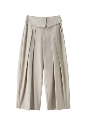 Femme portant des lunettes de soleil noires, une veste marron, un crop top noir, un pantalon beige large plissé avec une grande ceinture, et un collier chaîne doré.