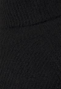 Svart stickad tyg med en strukturerad mönstring; har en ribbad halsdetalj och en mjuk, luddig yta för värme.