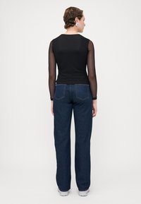 Svart langermet topp med gjennomsiktige ermer, sammen med høy midje blå denimjeans, med en rett benkutt og minimal baklommepynt.