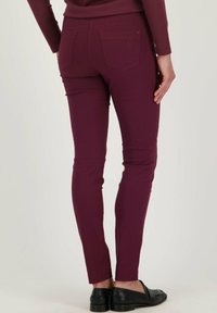 Bordeaux slim-fit broeken met een gladde textuur, voorzien van twee achterzakken en subtiele logo borduursels. Draagt met zwarte leren instappers.