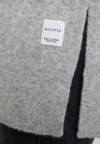 Šedý pletený svetr s texturovaným povrchem, s viditelnou štítkem s nápisem "Marc O'Polo DENIM" v modré barvě. Jednoduchý, čistý design bez vzorů.