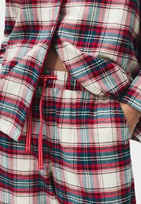 Pigiama a quadri rosso e blu realizzato in tessuto morbido; presenta una camicia dal taglio comodo e pantaloni corti con vita elastica e cordoncino.