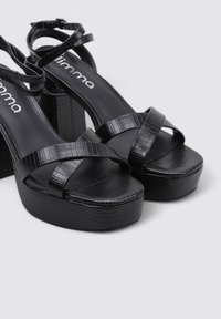 Sandalias de plataforma negras con correas de cuero texturizado y un tacón grueso. La plantilla es lisa y las correas presentan un diseño entrecruzado.