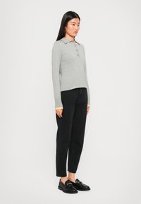 Polo shirt gris à manches longues avec un col jaune, trois boutons, poignets côtelés, porté avec un jean noir à jambe droite et des mocassins noirs.