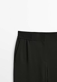 Pantalon taille élastique noir avec poches latérales, visible de la taille jusqu'au milieu des cuisses, sur fond blanc.