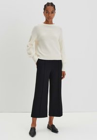 Maglione a maglia con texture cremosa, pantaloni neri a gamba larga e scarpe slip-on nere. L'outfit presenta una vestibilità comoda e un design semplice.