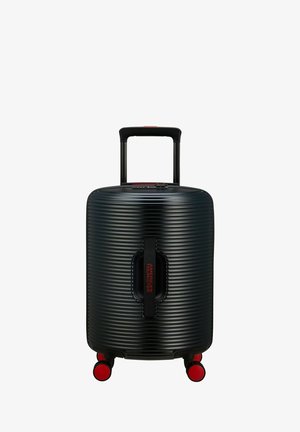 Valise noire à coque dure avec texture à rainures verticales, poignée télescopique et quatre roues rouges pour la mobilité. Comprend un logo sur la poignée.