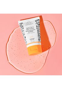 White tube of Drunk Elephant Beste No. 9 Jelly Cleanser with black geometric patterns and orange flip cap on pink background with gel splash.