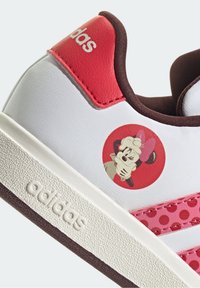 Białe sneakersy Adidas z czerwonymi akcentami, w wzór w kropki, z grafiką postaci w czerwonym okręgu z boku.
