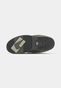 Black and olive sneaker sole with textured rubber, hexagonal patterns, and a midsole logo label. Features cushioning and grip details.