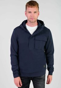 Sudadera de marina con capucha, con un bolsillo delantero estilo canguro, hecha de tela suave. Presenta una cremallera y puños acanalados. Lleva puesta sobre una camiseta blanca.