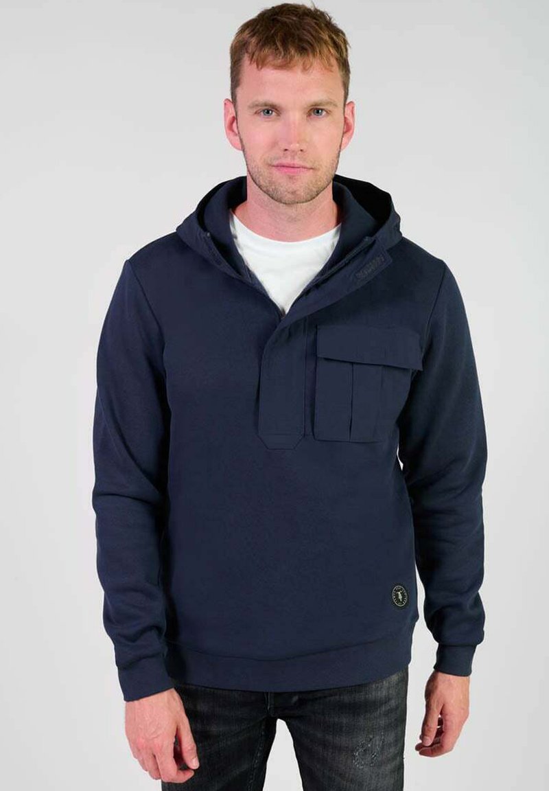 Sudadera de marina con capucha, con un bolsillo delantero estilo canguro, hecha de tela suave. Presenta una cremallera y puños acanalados. Lleva puesta sobre una camiseta blanca.