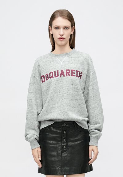 Γκρι φούτερ με μοβ κεντημένο λογότυπο "DSQUARED2", άνετη εφαρμογή, και ριμπ μανσέτες, συνδυασμένο με μαύρη δερμάτινη φούστα με κουμπιά ως διακοσμητικό στοιχείο.