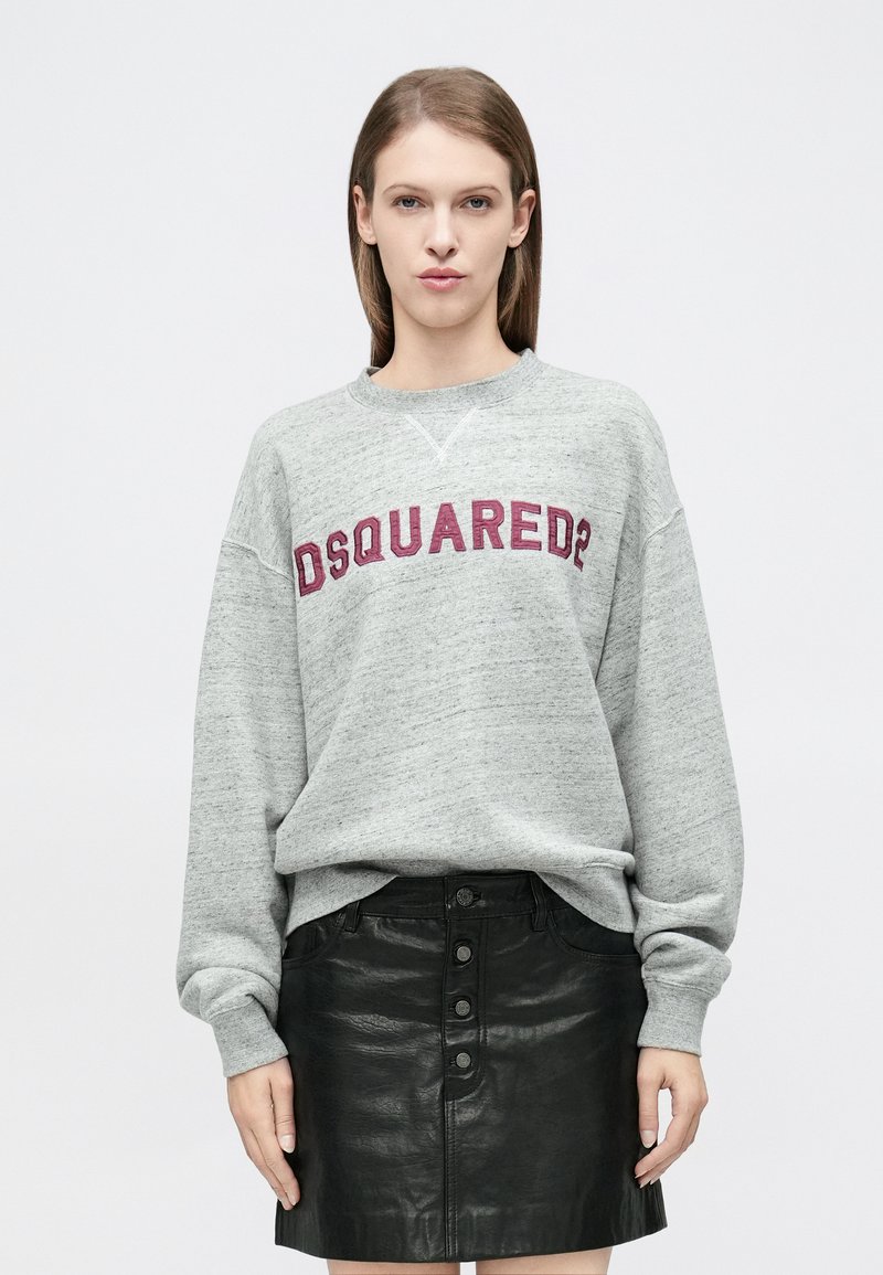 Pelēks sporta krekls ar violetā izšuvuma "DSQUARED2" logotipu, brīva piegriezuma un ribotiem aprocēm, kombinēts ar melnu ādas svārku ar pogas detaļu.