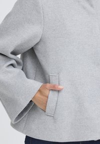 Grå føltejakke med afslappet pasform, brede ærmer og en indsatre lomme i sidesømmen for funktionel detalje.