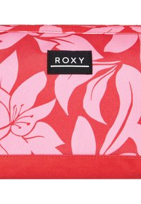 Red fabric accessory featuring pink floral patterns. A black label with "ROXY" is stitched on, adding contrast to the design.