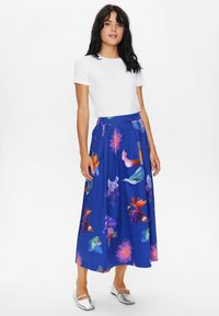 Der blaue Maxikilt mit Blumenmuster zeigt lebhafte Designs mit orangefarbenen, rosa und grünen Akzenten; kombiniert mit einem schlichten weißen T-Shirt und silbernen Ballerinas.