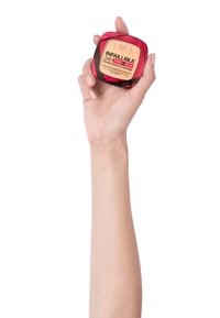 Fond de teint en poudre L'Oréal Infallible 24H Fresh Wear dans une boîte ronde avec des accents rouges et noirs, tenue dans une main. Texture lisse, teinte beige clair.