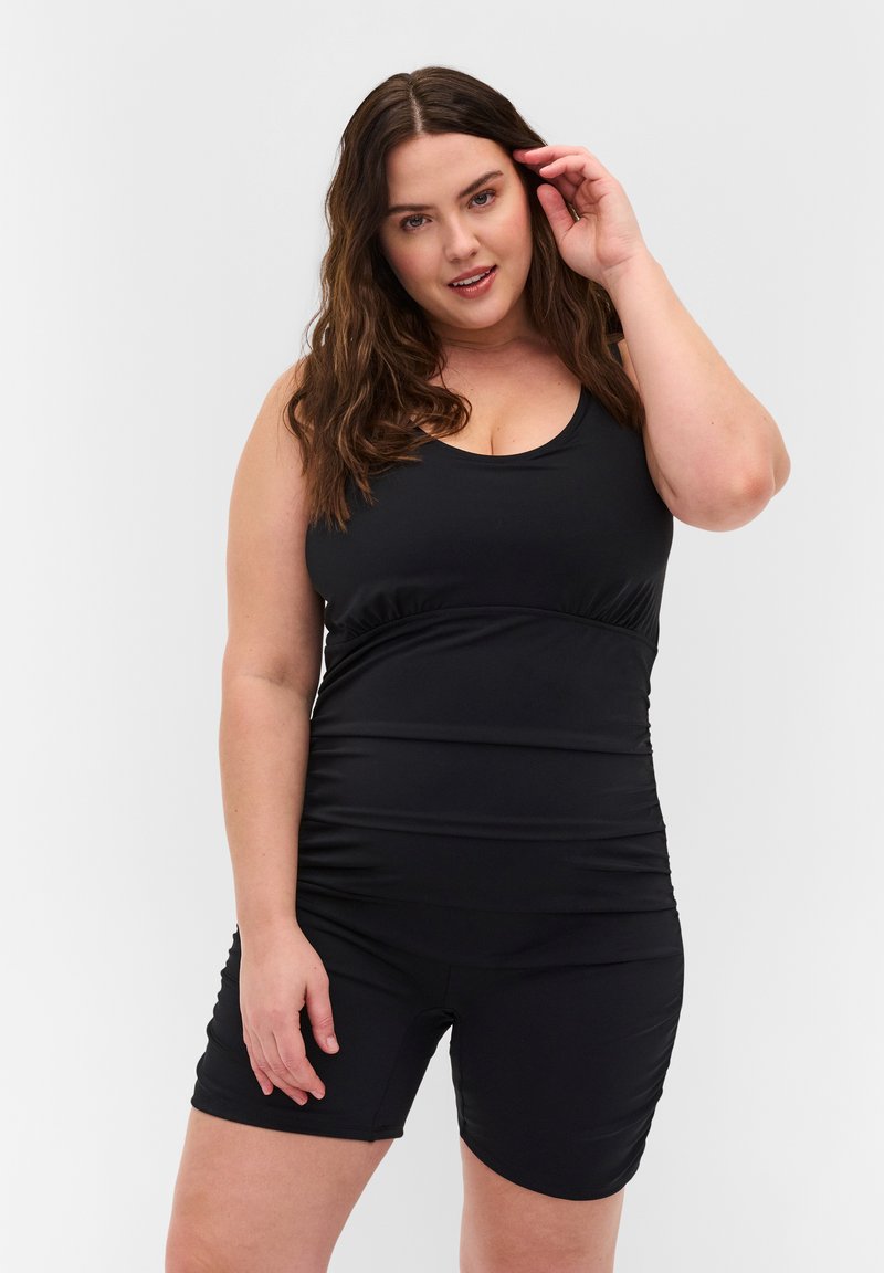 Combinaison athlétique noire avec un décolleté en scoop, des détails froncés à la taille et de petites jambes pour le confort et la mobilité.