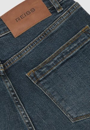 Denimjeans i en mørk vask med et lædermærke med brandet "REISS." Indeholder kontrasterende gule syninger og en baglomme.