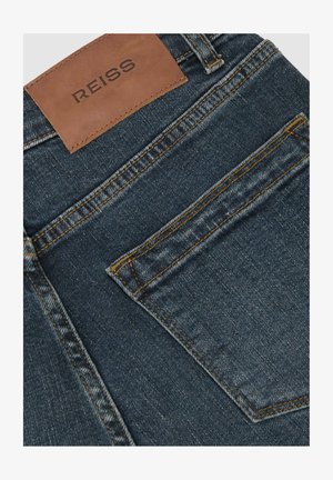 Dunkelblaue Jeans aus Denim mit einem Lederetikett, auf dem "REISS" steht. Verfügt über kontrastierende gelbe Nähte und eine Gesäßtasche.