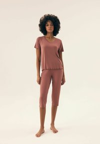 Lekki, różowy zestaw wypoczynkowy składający się z koszulki z krótkim rękawem i dekoltem w serek oraz spodni do kolan z falbaną. Miękka tekstura, dopasowany krój.