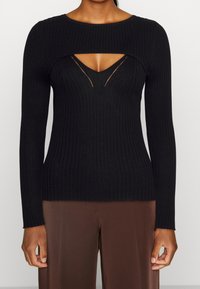 Haut noir à manches longues à côtes avec un design découpé au niveau du col. Fabriqué en tissu doux et texturé avec une silhouette ajustée.
