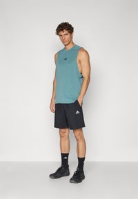 Turkisærmeløs top, sorte shorts, sorte atletiske sko med Adidas-logoet i flere placeringer, glat stof, tætsiddende design.