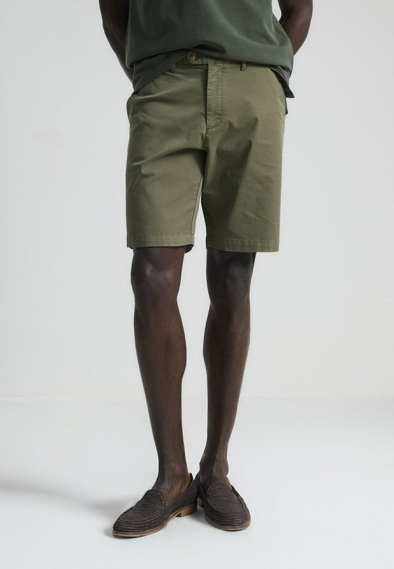 Pantalones cortos verde oliva con un corte clásico, material de algodón y una textura suave. Presentan un cierre con botón y bolsillos laterales.