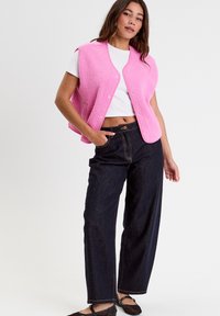 Pink fleece vest with snap buttons, worn over a white t-shirt and paired with dark denim wide-leg pants and black mesh flats.